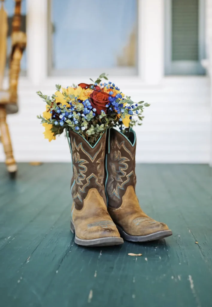 A worn pair of cowboy boots sits on a porch with colorful flowers sticking out of them at Old Coon Creek Wedding Venue in Beloit, Wisconsin