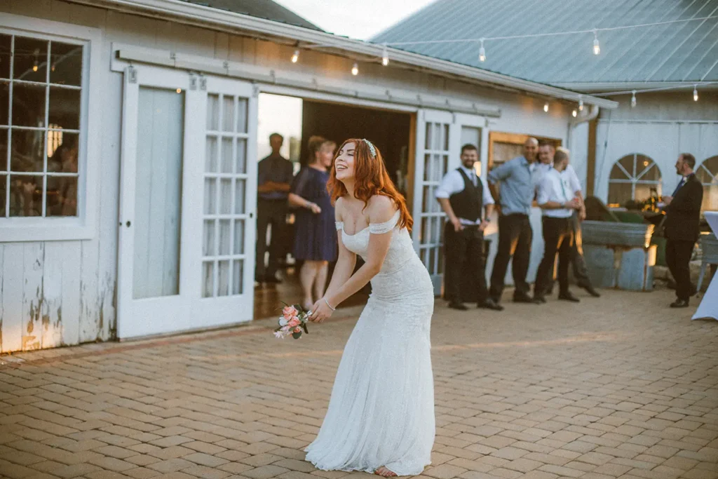 A bride prepares to throw her bouquet on the patio at Old Coon Creek while friends and family observe at a Wedding Venue in Beloit, Wisconsin