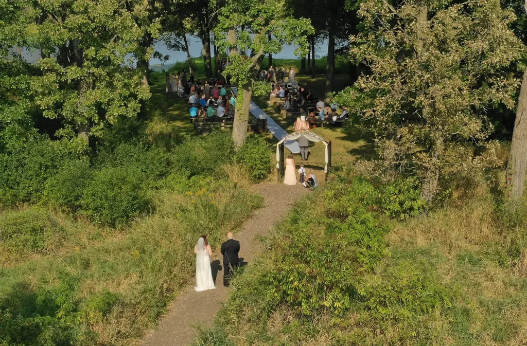 An aerial view of the Old Coon Creek waterfront ceremony site during a waterfront wedding with friends and family gathered at Old Coon Creek Wedding Venue in Beloit, Wisconsin