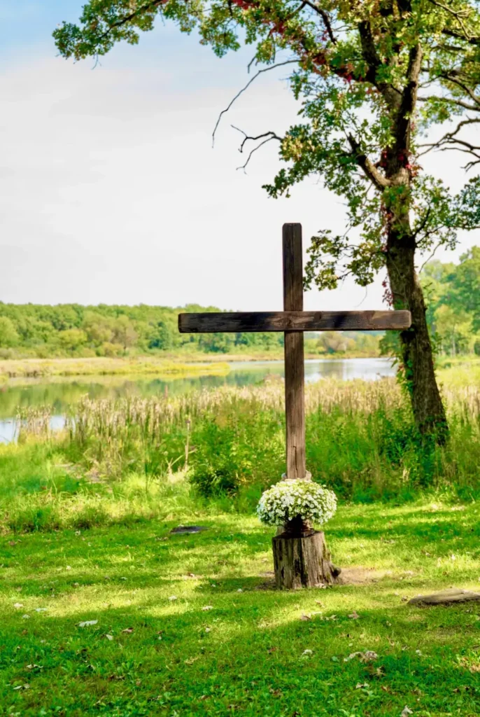 A Christian wooden cross is shows sitting near the water of the waterfront ceremony site at Old Coon Creek Wedding Venue in Beloit, Wisconsin