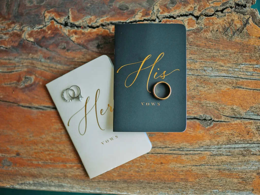 His and hers wedding vows and bride and groom's rings are shows sitting on a rustic surface at Old Coon Creek Wedding Venue in Beloit, Wisconsin