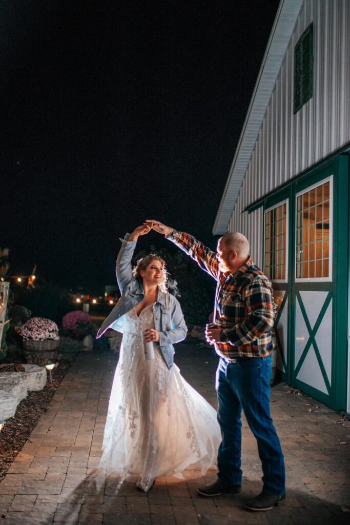 A bride and groom twirl outdoors during their reception at the old rustic barn at Old Coon Creek Wedding Venue in Beloit, Wisconsin