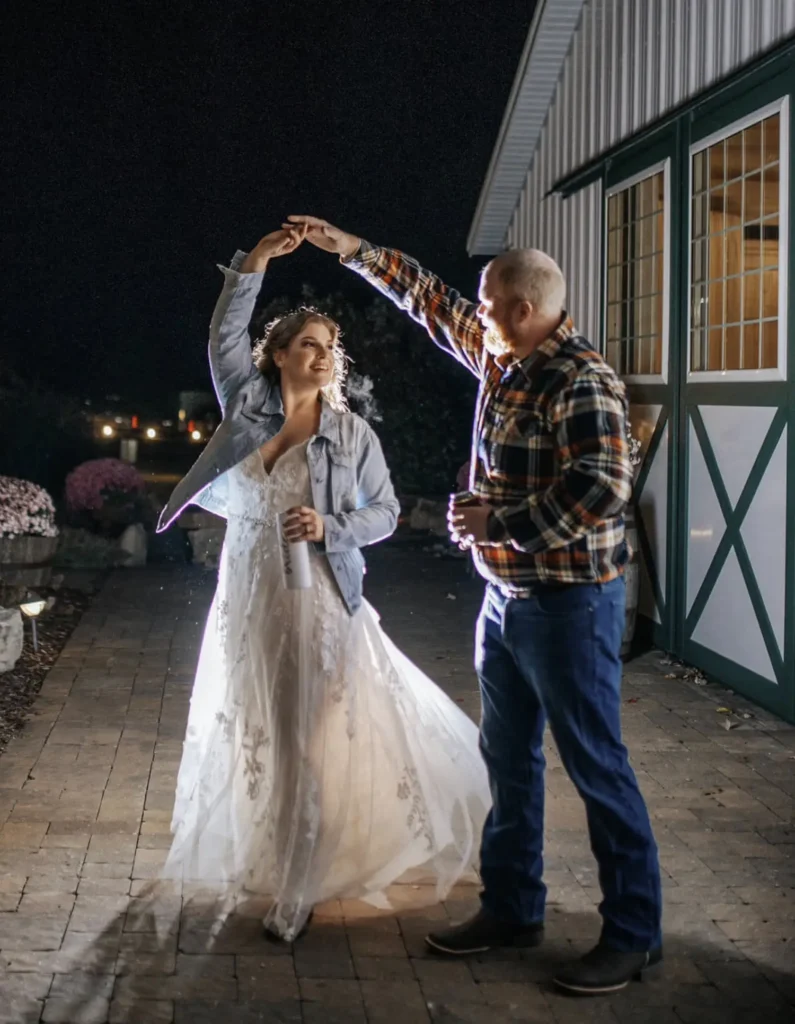 A bride and groom twirl outdoors during their reception at the old rustic barn at Old Coon Creek Wedding Venue in Beloit, Wisconsin