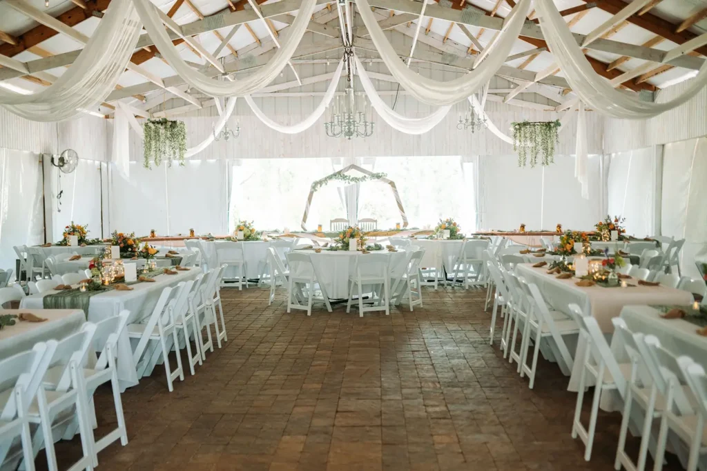 A wide view of the interior of the pavilion with white chairs and white decorations before a wedding reception at Old Coon Creek Wedding Venue in Beloit, Wisconsin