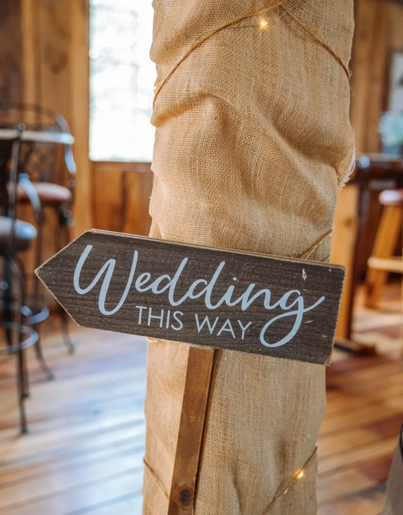 A sign reading Wedding This Way is propped up inside the rustic barn at Old Coon Creek Wedding Venue in Beloit, Wisconsin